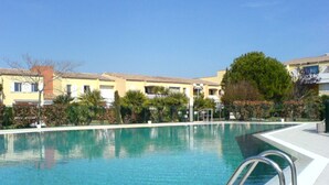 Una piscina limpida con una scaletta in metallo, circondata da un'area verde alberata e un edificio con tetto in tegole.