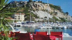 Una marina con barche ormeggiate, una scogliera con edifici e sedie rosse in primo piano.