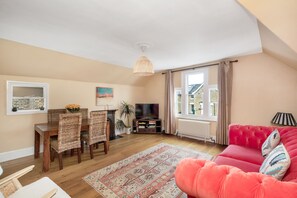 A living room with a wooden dining table, chairs, a sofa, a TV, and a large window with curtains. - Lovely 2BR, Richmond Hill & Parking (Richmond upon Thames)