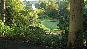 A lush garden with a variety of trees and shrubs, a well-maintained lawn, and a distant building. - Lovely 2BR, Richmond Hill & Parking (Richmond upon Thames)
