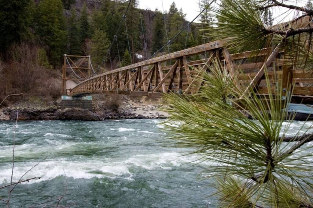 A wooden bridge over a fast-flowing river with a forested background.