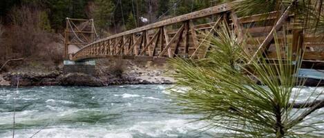 A wooden bridge over a fast-flowing river with a forested background.