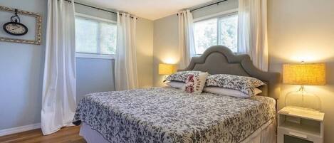 Ein Schlafzimmer mit Bett, Nachttisch, Lampe, Deckenventilator und einem Fenster mit Vorhängen.