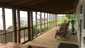 Eine überdachte Holzterrasse mit Blick auf das Wasser, Holzstühle und ein Tisch.