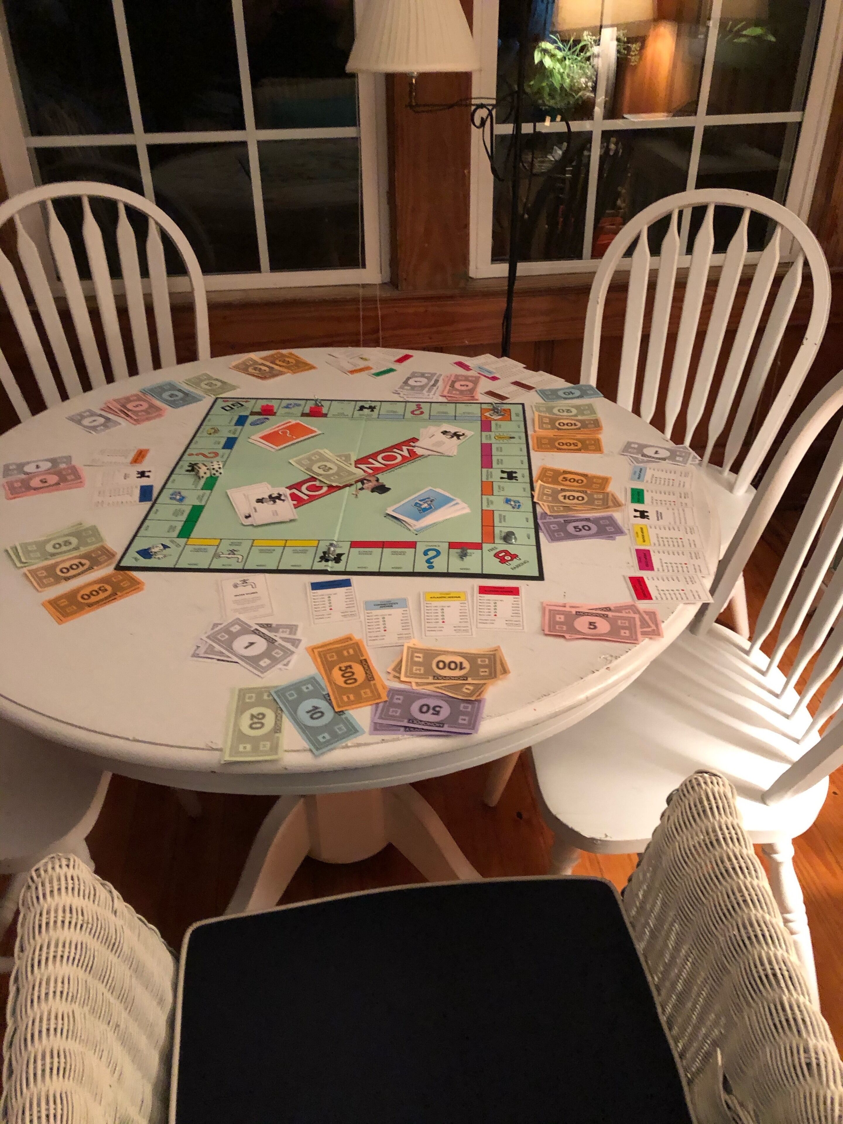 A Monopoly game in progress on a round white table surrounded by white chairs.