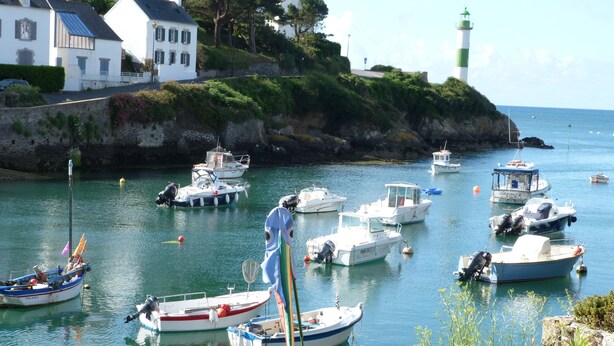 A harbor with various boats docked, a lighthouse in the background, and houses along the coastline. - The home of the Moulin de Kérangoc (Melgven)