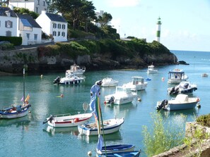 A harbor with various boats docked, a lighthouse in the background, and houses along the coastline.