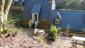 A rustic stone building with a steeply pitched roof, a wooden staircase leading to a door, and a small window. - The home of the Moulin de Kérangoc (Melgven)