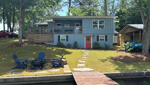 A two-story house with a red door, a covered porch, and a small dock extending into a pond.