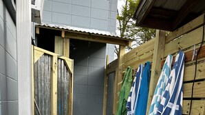 A wooden deck leading to a wooden structure with a door, surrounded by a grey wall and a wooden fence.