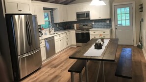 A modern kitchen with white cabinets, stainless steel appliances, and a wooden dining table.