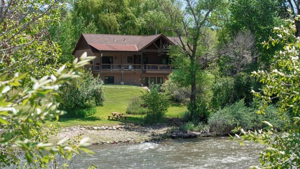 Een lodge met een balkon met uitzicht op een rivier, omgeven door weelderig groen.