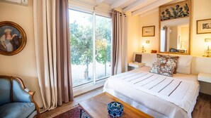 Ein Schlafzimmer mit einem großen Bett, einem Sessel, einem Fenster mit Vorhängen und einem Gemälde an der Wand.