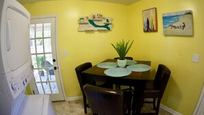 A dining area with a table set for four, a potted plant, and a painting on the wall.