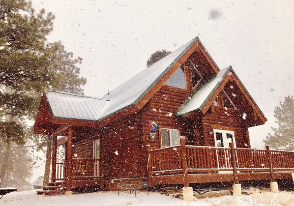 Una cabaña de madera con un porche y un techo cubierto de nieve.
