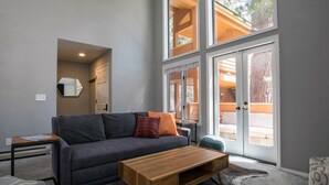 A modern living room with a grey sofa, wooden coffee table, and a large sliding glass door leading to an outdoor area. - Cozy Updated McCloud Condo - Walk to Lakeshore Drive, Shops & Restaurants (Incline Village)