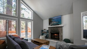 A modern living room with a stone fireplace, a large window, and a view of the outdoors. - Cozy Updated McCloud Condo - Walk to Lakeshore Drive, Shops & Restaurants (Incline Village)