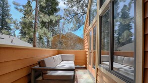 A wooden deck with a bench and a table, large windows offering a view of pine trees. - Cozy Updated McCloud Condo - Walk to Lakeshore Drive, Shops & Restaurants (Incline Village)