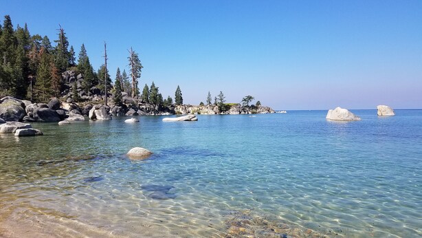 A clear lake with visible rocks and trees around the shore. - Cozy Updated McCloud Condo - Walk to Lakeshore Drive, Shops & Restaurants (Incline Village)