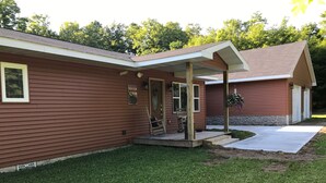 A two-story house with a covered porch, a stone foundation, and a well-maintained lawn. - In The Heart Of The Hiawatha National Forest ~ Easy Access To The Trail System (Shingleton)