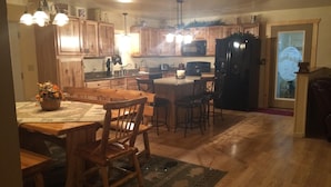 A kitchen with wooden cabinets, a dining table with chairs, a refrigerator, and a microwave. - In The Heart Of The Hiawatha National Forest ~ Easy Access To The Trail System (Shingleton)