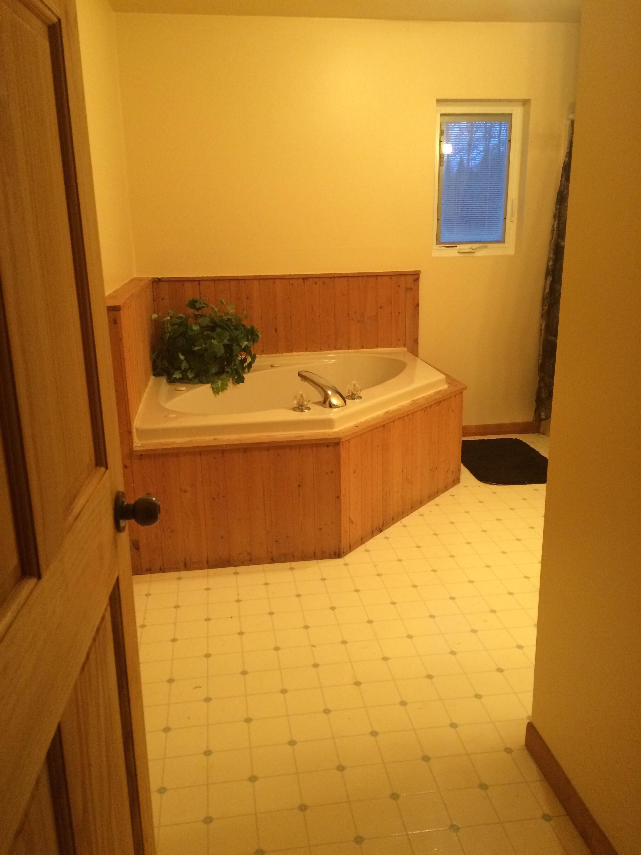 A bathroom with a freestanding bathtub, wooden paneling, a window, and a tiled floor.