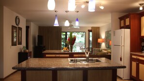 Cozinha com ilha central, geladeira e área de refeições com sofá e mesa.