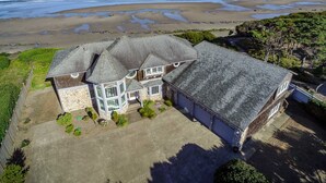Une grande maison à deux étages, dotée d’une façade en pierre et de plusieurs toits à pignons, située en bord de mer et offrant une vue sur l’océan.