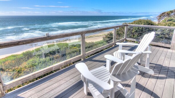 Une terrasse avec deux chaises Adirondack blanches donnant sur une plage et l’océan.