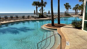 A clear blue pool with a 3 FT depth marker, surrounded by lounge chairs and palm trees, overlooking a beach.