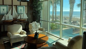 A spacious living room with a large window overlooking the ocean, featuring a comfortable seating area and a wooden coffee table.