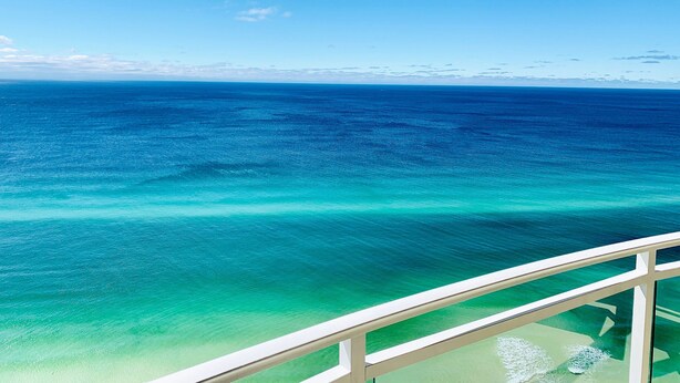 A clear view of the ocean from a balcony with a glass railing.