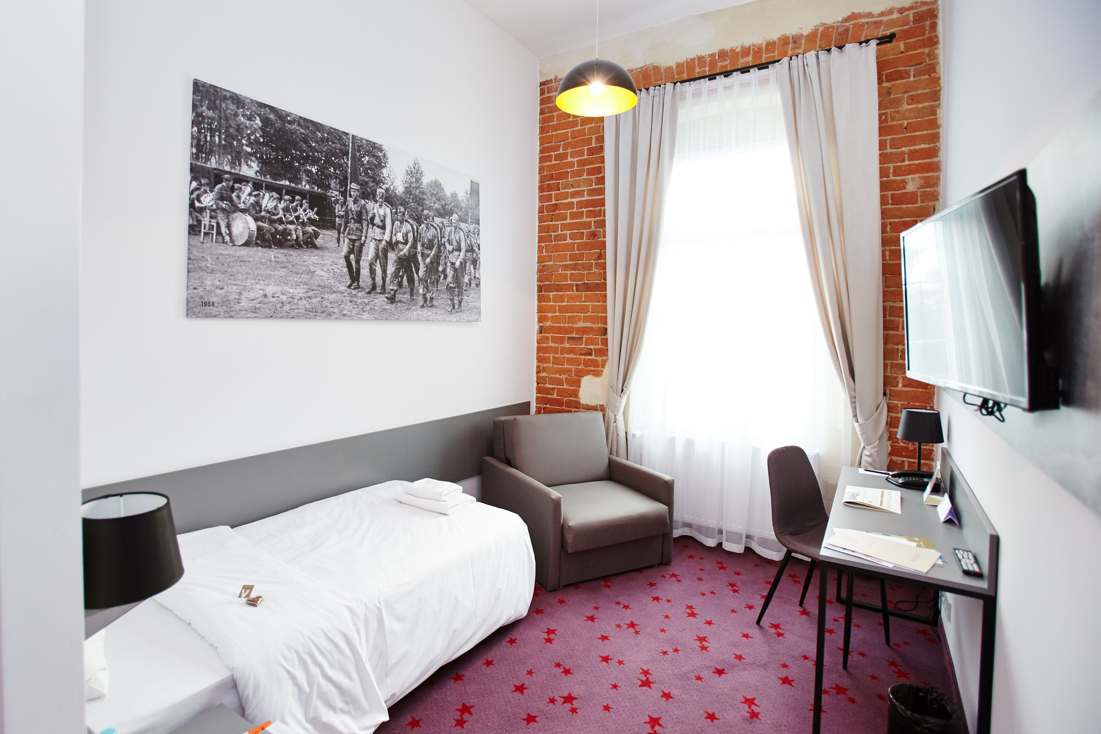 A hotel room with a bed, a desk, a chair, a television, and a picture on the wall.