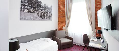 A hotel room with a bed, a desk, a chair, a television, and a picture on the wall.