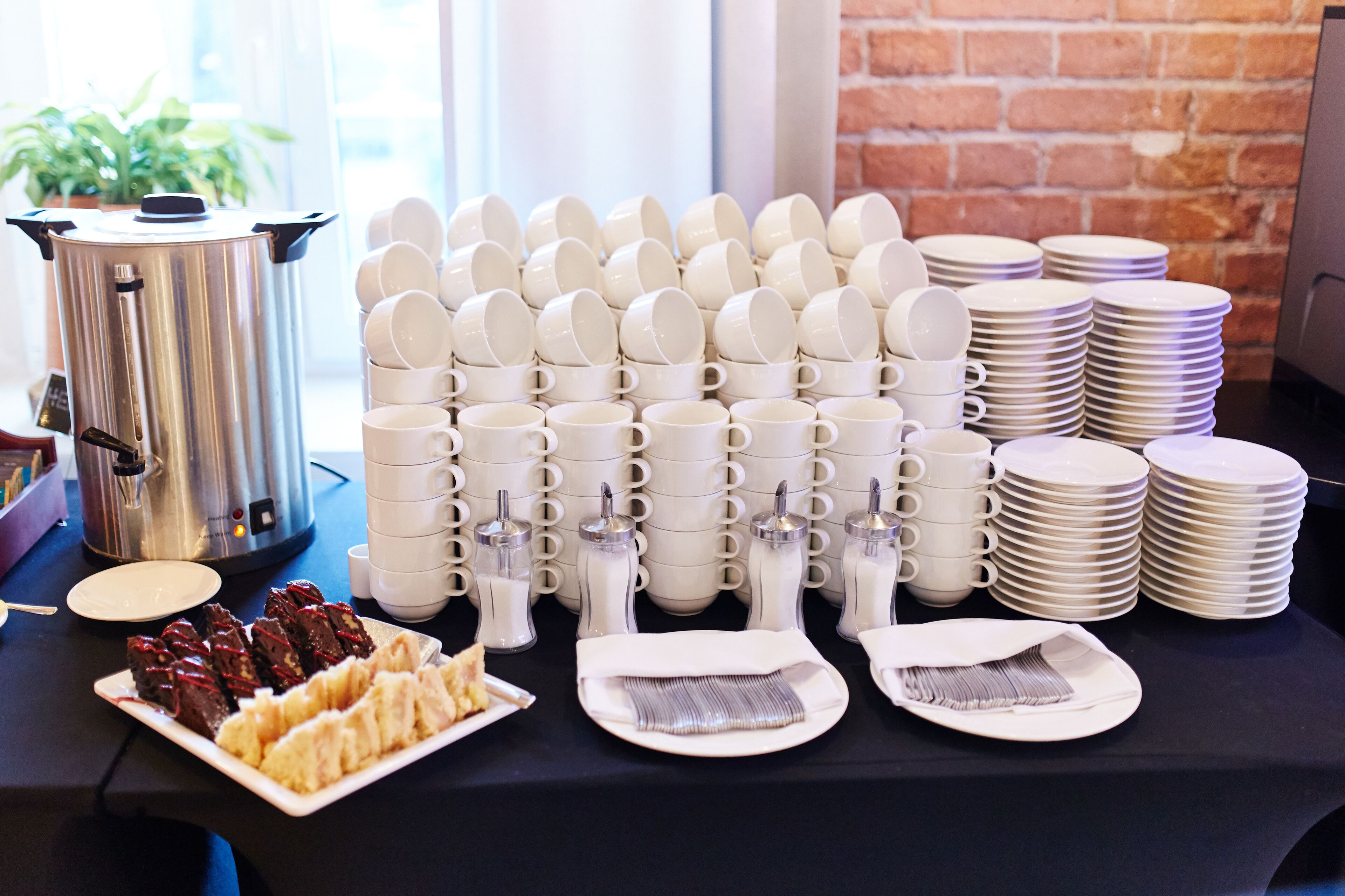 A table with stacks of white cups, plates, and a silver pot, likely for a breakfast service.