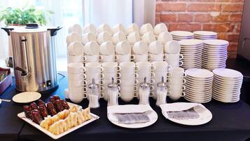 A table with stacks of white cups, plates, and a silver pot, likely for a breakfast service.