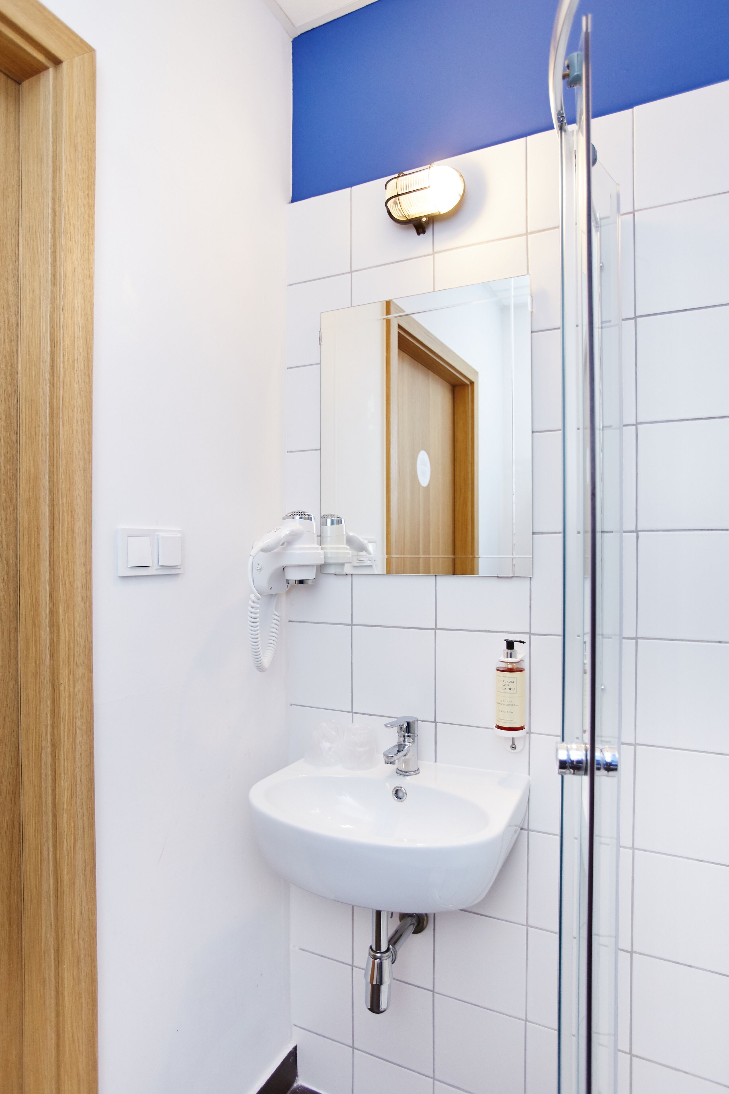 Une salle de bain avec un lavabo blanc, une cabine de douche en verre et une porte en bois.