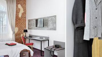 A hotel room with a bed, desk, chair, and a coat rack with clothes.
