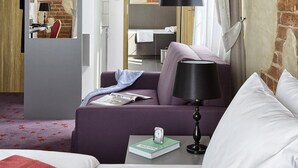 A hotel room with a brick wall, a bed, a sofa, a desk, and a mirror. - Koszary Arche Hotel (Gora Kalwaria)
