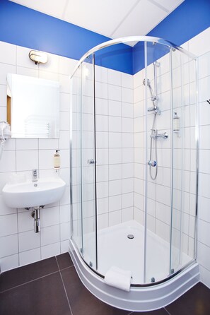 A modern bathroom with a glass-enclosed shower, white tiles, a sink, and a mirror. - Koszary Arche Hotel (Gora Kalwaria)