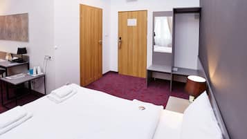 Habitación de hotel con cama, escritorio con lámpara, silla, armario y espejo.