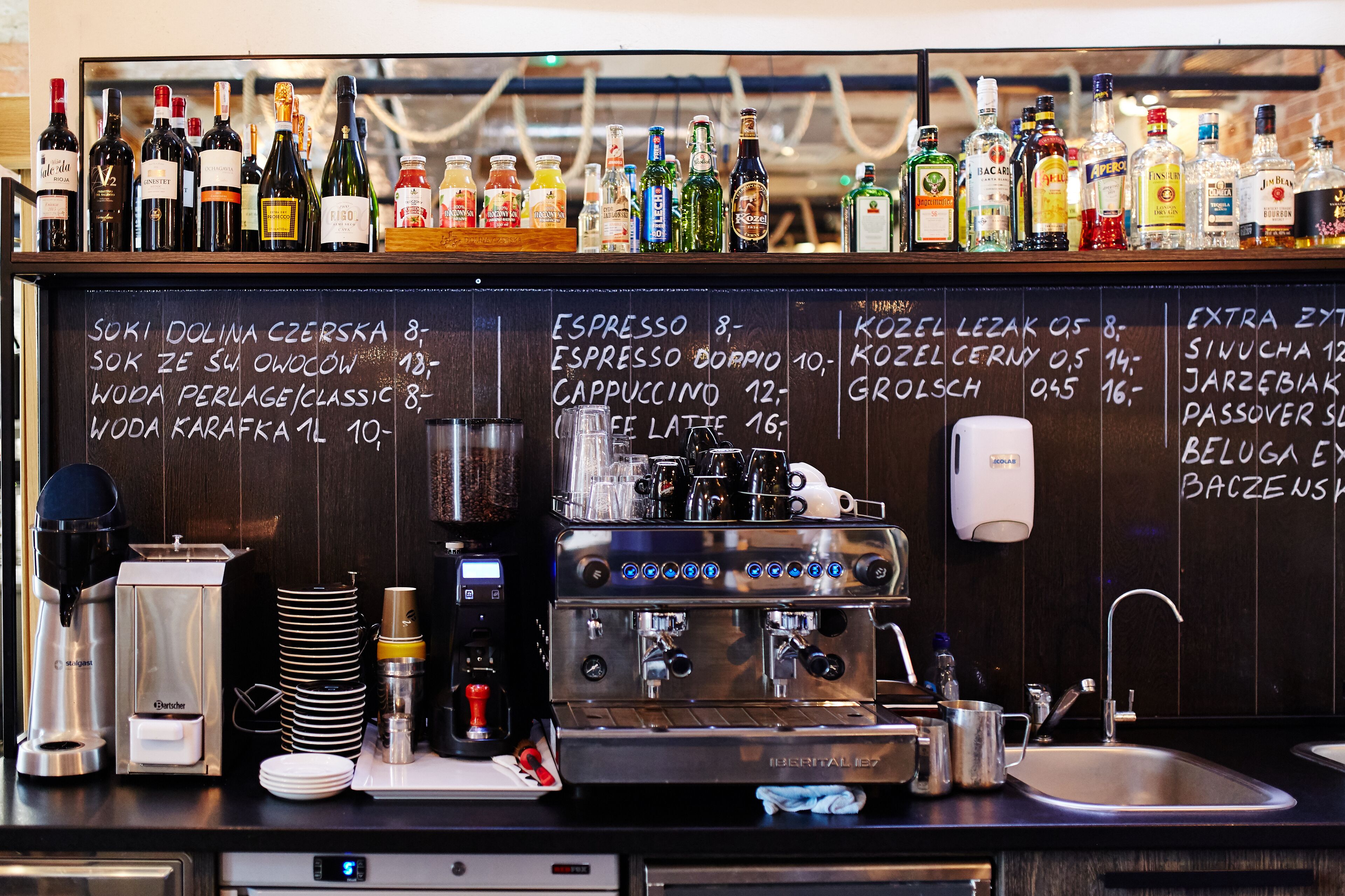Eine Barbereich mit Kaffeemaschine, Spüle und einer Auswahl an Flaschen in Regalen.
