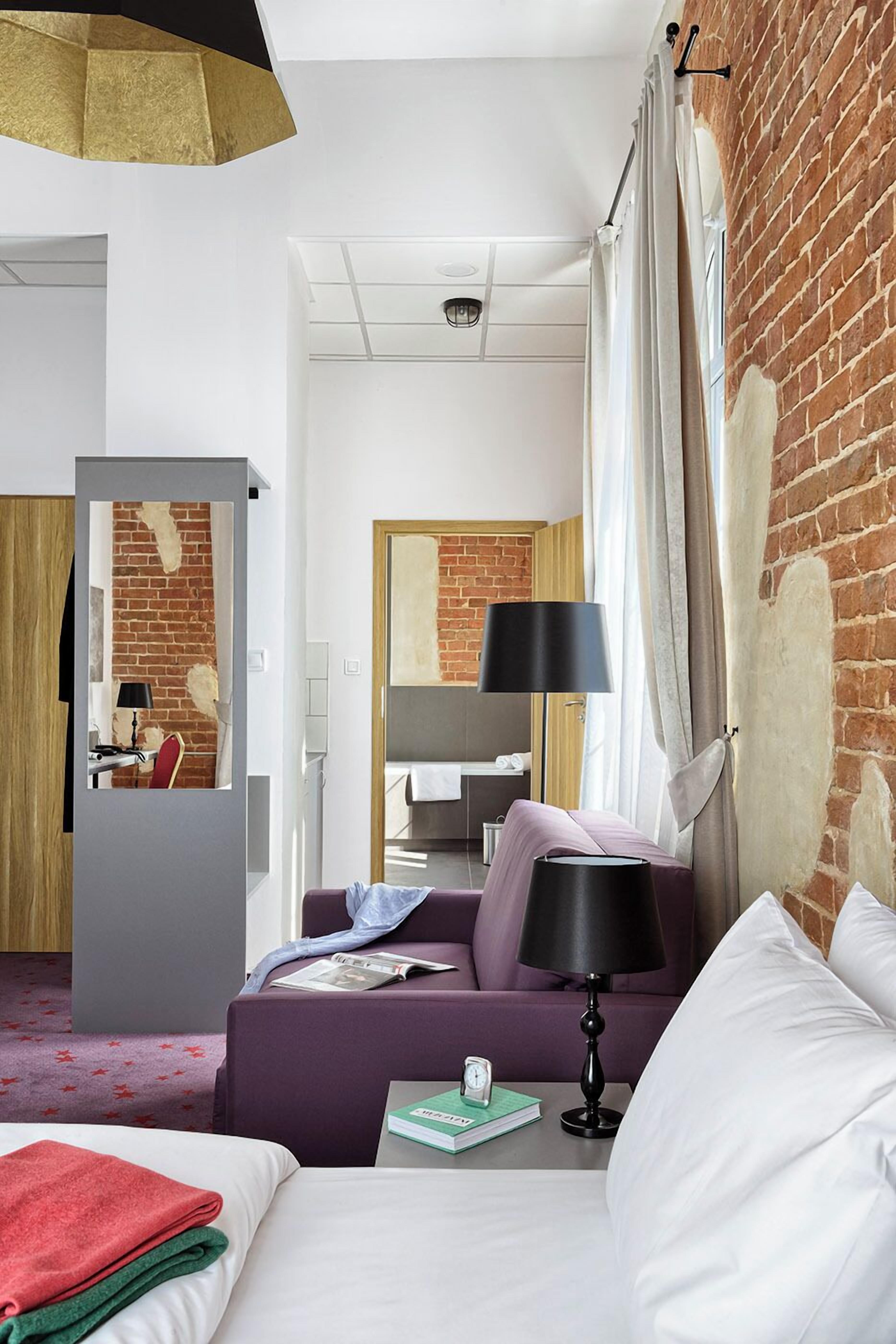 Una habitación de hotel con pared de ladrillo, cama, sofá, escritorio y espejo.
