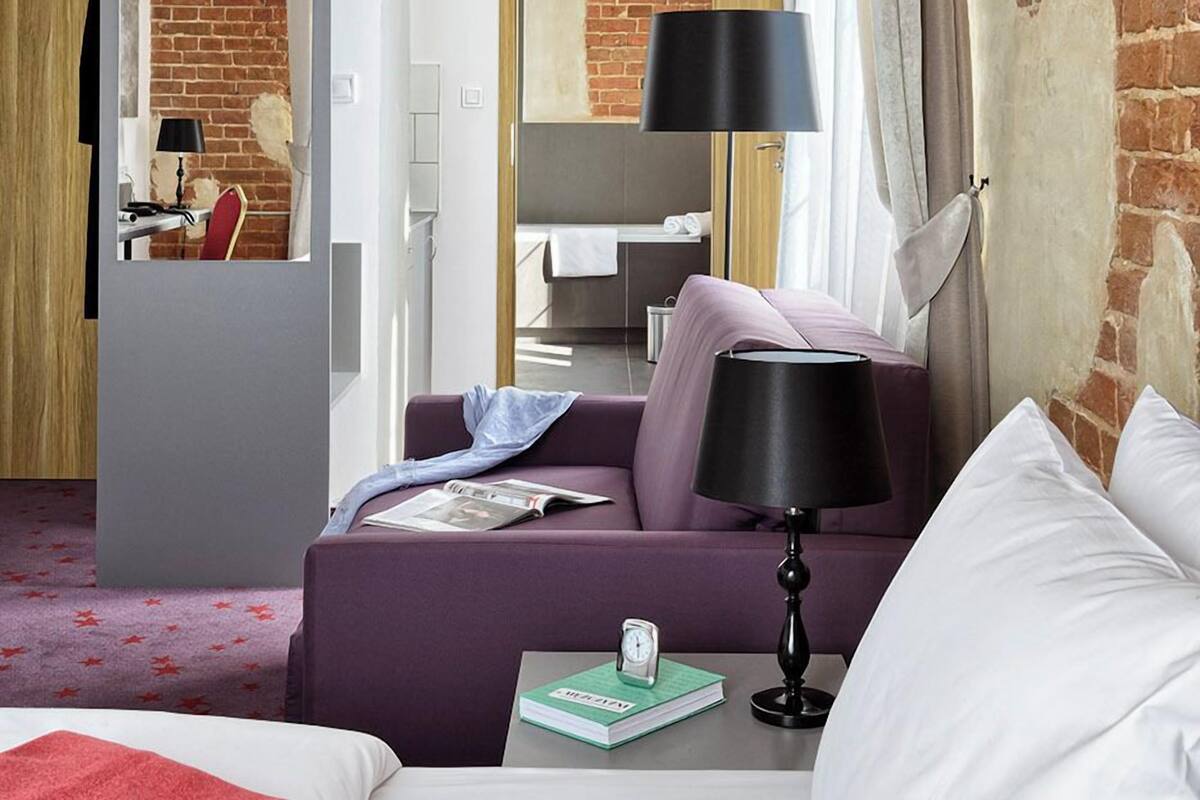 A hotel room with a brick wall, a bed, a sofa, a desk, and a mirror.