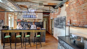 A bar area with a brick wall, bar stools, and a counter with a bartender. - Koszary Arche Hotel (Gora Kalwaria)