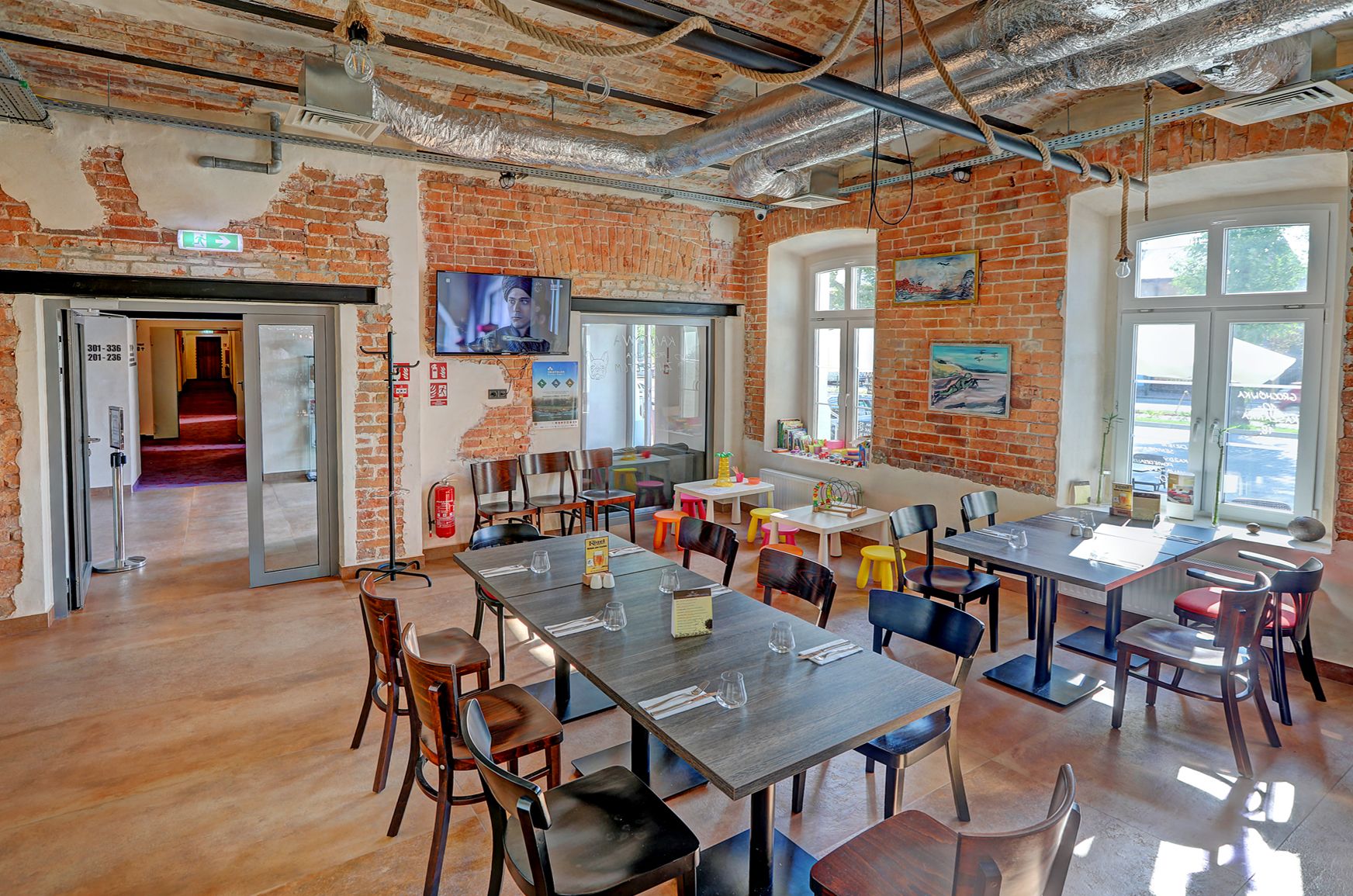 A restaurant with brick walls, wooden tables, and chairs. There are windows and a TV mounted on the wall.