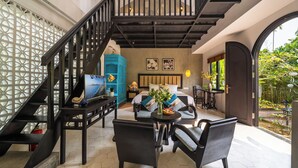 A spacious living area with a staircase, a blue cabinet, a bed with blue and white bedding, and a dining table with chairs. - Nghe Garden Resort (Da Nang)