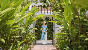 A woman in a blue dress standing in a garden pathway leading to a building with a red roof. - Nghe Garden Resort (Da Nang)