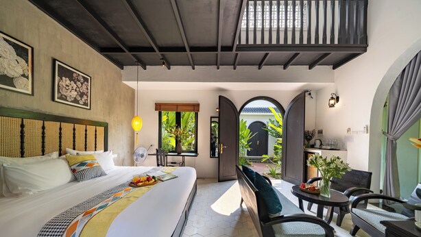 A bedroom with a bed, bedside table, and a view of the garden. - Nghe Garden Resort (Da Nang)