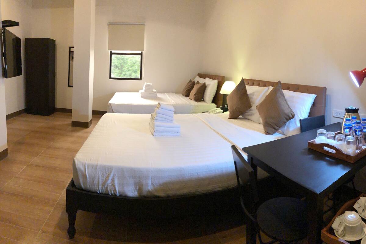 A hotel room with two beds, a desk with a tray of toiletries, and a TV mounted on the wall.